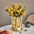 Vase doré avec bouquet de fleurs jaune posé sur une table blanche.