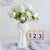 Vase en forme de coeur blanc avec bouquet de fleurs blanches posé sur une table blanche.