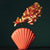 Vase en forme de coquillage rouge avec fleurs rouges posé sur une table.