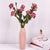 Vase en résine origami rose avec bouquet de fleurs rouge posé sur une table blanche.