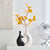 Vase noir et blanc duo coeur avec fleurs posé sur une table blanche.