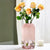 Vase rose avec bouquet de roses orange sur une une table blanche.