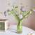 Vase transparent avec bouquet de fleurs posé sur une table blanche.