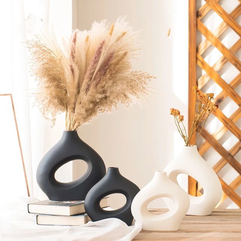 Vases design en forme de donuts noir et blanc avec fleurs séchées sur une table.