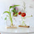 Vases Soliflores Sphérique Transparent sur Socle en Bois, présentation de deux modèles avec fleurs et plantes vertes sur une table blanche.