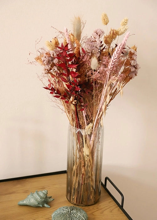 Présentation d'un vase transparent avec bouquet de fleurs séchées, posé sur un plateau en bois, mise en scène.