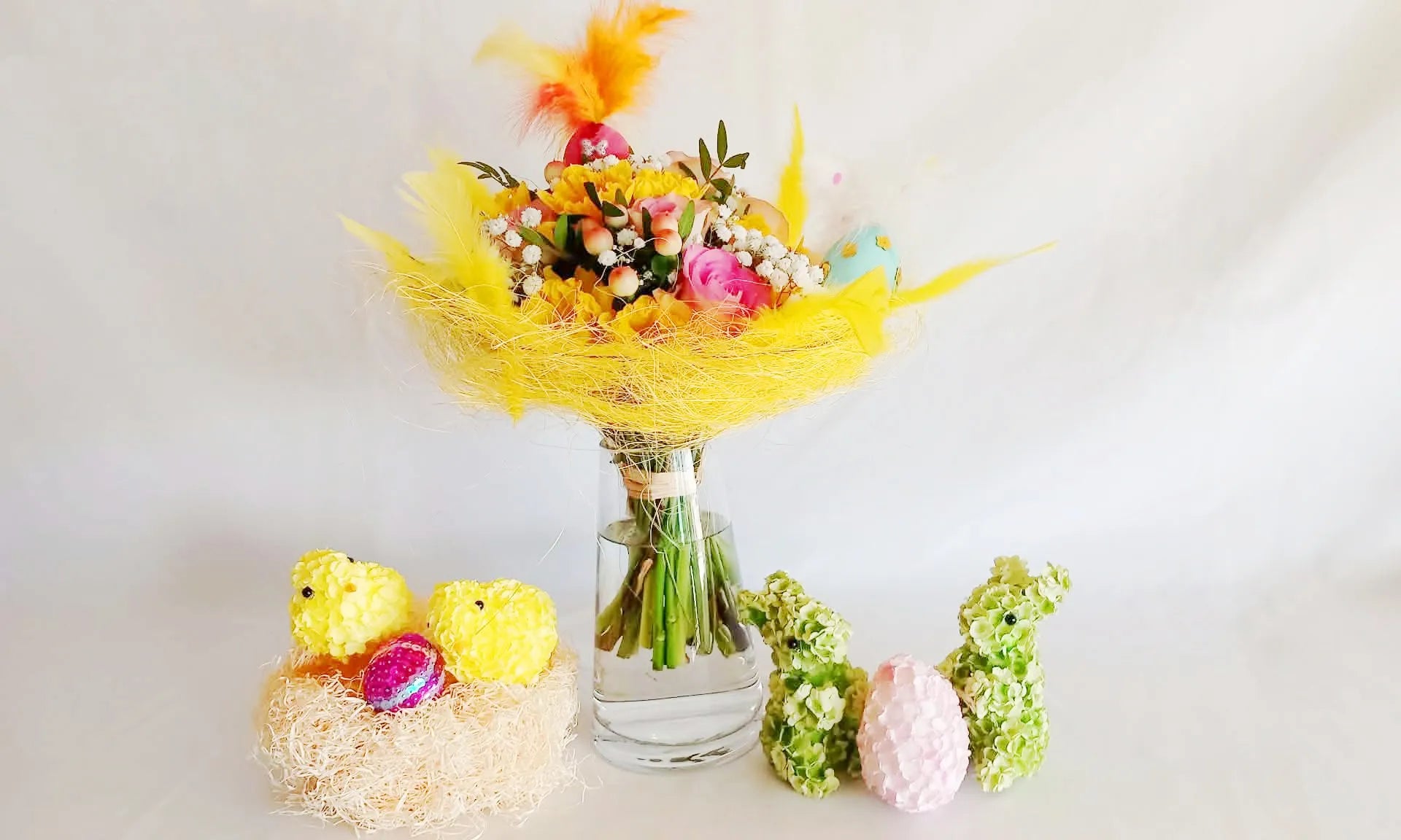 Présentation d'un vase en verre transparent avec un de bouquet de fleurs et ornements de Pâques.