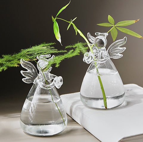 Soliflore Ange transparent en Verre, présentation de deux anges avec tiges vertes, mise en scène sur une table avec un livre blanc.