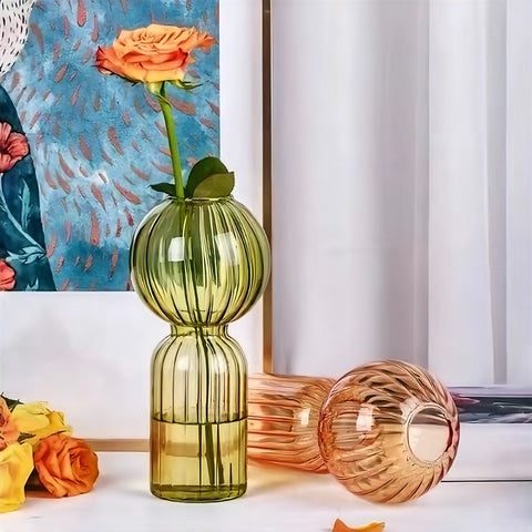 Soliflore forme bilboquet coloré en verre, présentation des modèles vert avec fleurs et ambre couché sans fleurs sur une table.