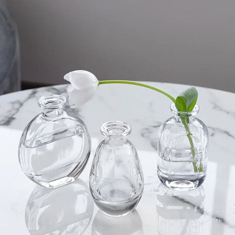 Soliflore forme petit flacon transparent en verre présentation des modèles A , B  et C avec fleurs sur table en marbre