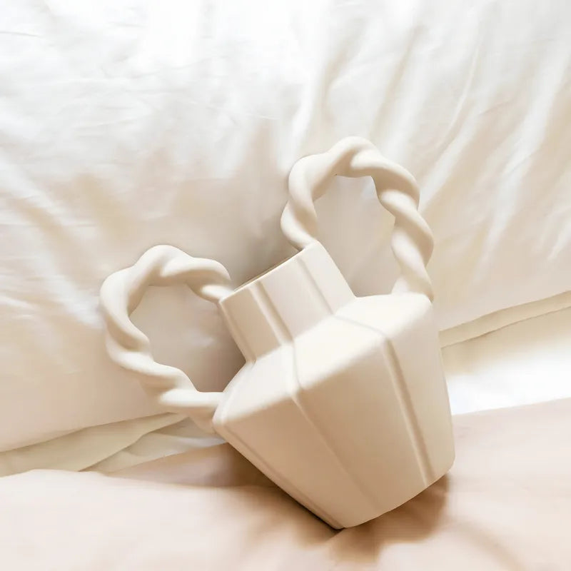 Vase Amphore Moderne Anses présentation du modèle beige couché sur un canapé blanc.