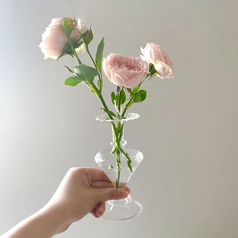 Vase carafe chic transparent en verre tenu en main avec fleurs.