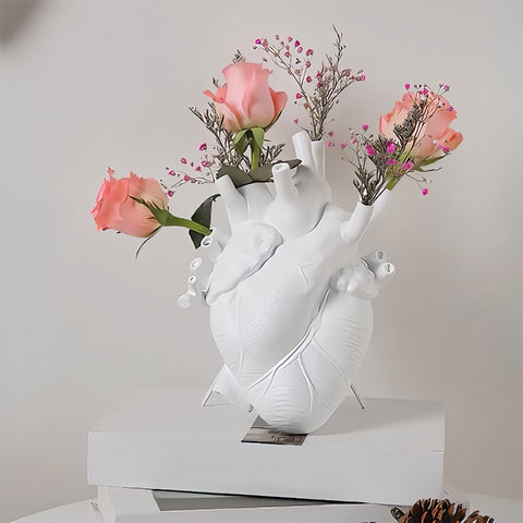 Vase cœur humain blanc en céramique avec roses et fleurs sur une pile de livre et sur une table