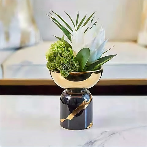 Vase coupelle noir et doré en céramique présentation sur une table avec fleur blanche et feuillages verts.