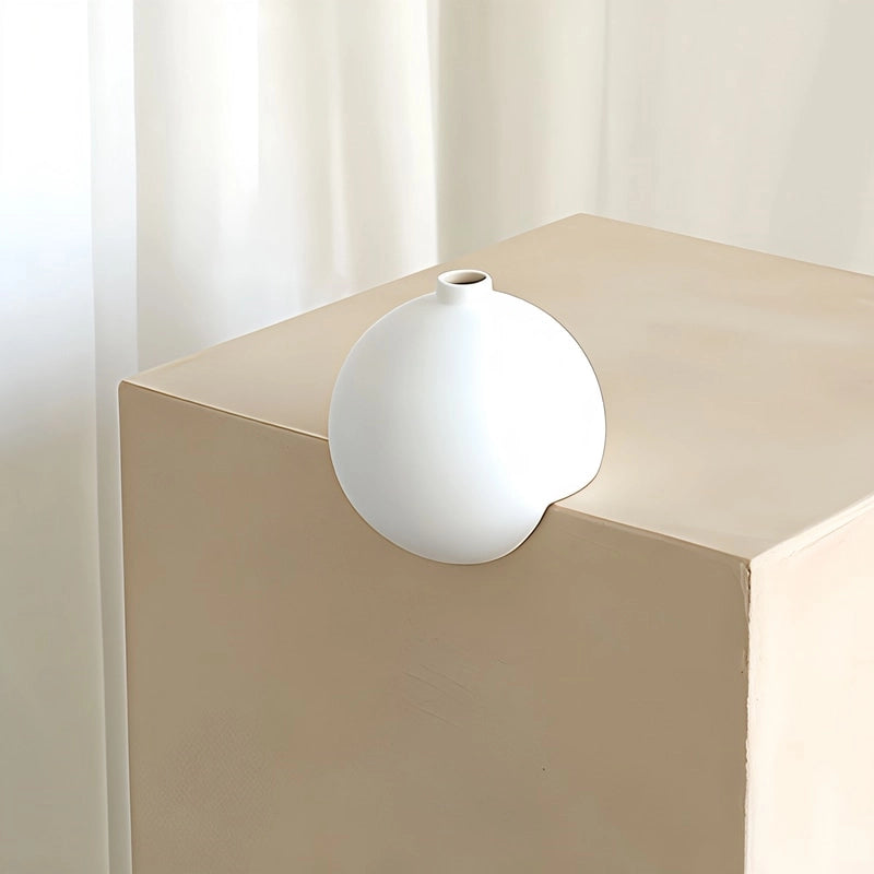 Vase Moderne Sphérique à Angle Droit Blanc en Céramique présentation sans fleurs, posé sur l'angle d'un meuble beige.