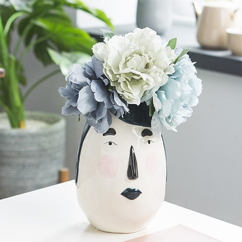 Vase ovale blanc visage original en céramique présentation avec bouquet de fleurs sur une table
