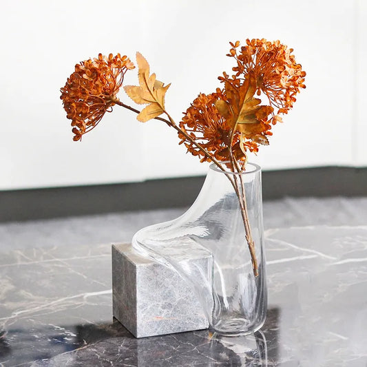 Vase transparent effet fondu sur cube en marbre, présentation avec fleurs séchées sur une table en marbre.
