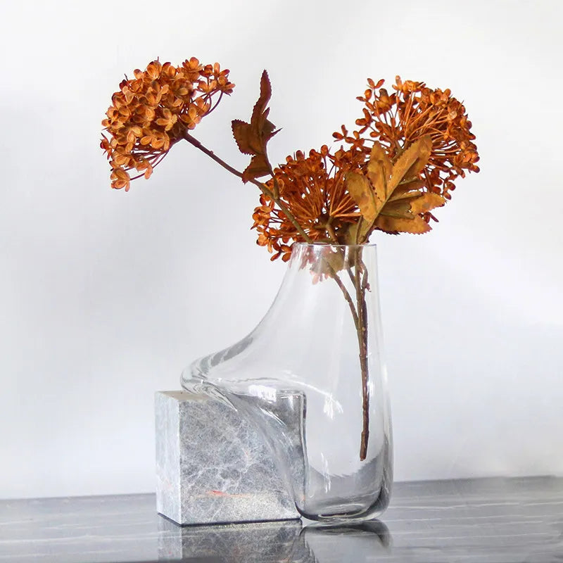 Vase transparent effet fondu sur cube en marbre, présentation avec fleurs séchées sur une table.