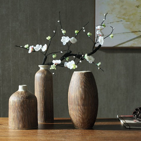 Vase artisanal marron aspect écorce rayée en Céramique, présentation des styles A avec tige à fleurs blanches, C et B vides, placés sur un centre de table.