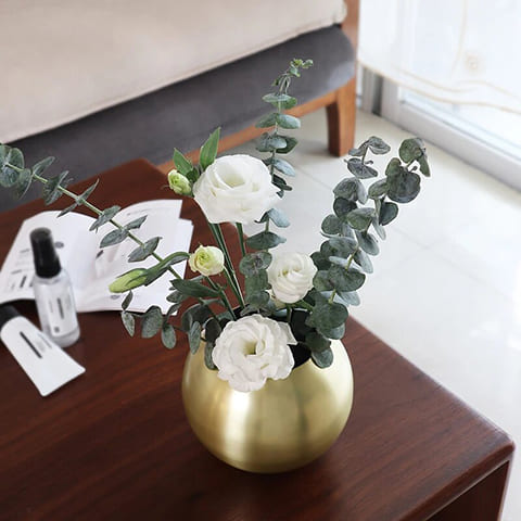 Vase sphérique moderne design raffiné, présentation modèle Or Avec roses blanches et tiges d'eucalyptus sur une table de nuit.